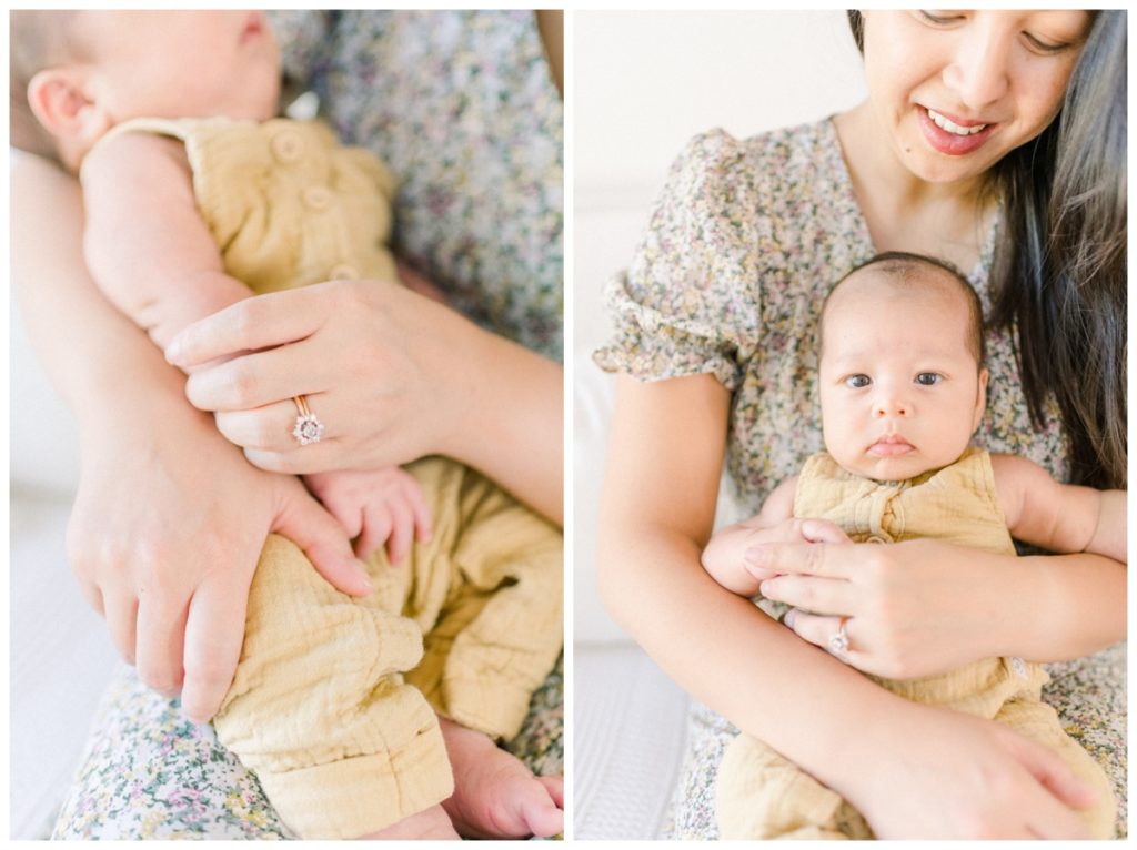 A close up photo of a mom holding her newborn son wearing a light yellow onesie holding his hand.