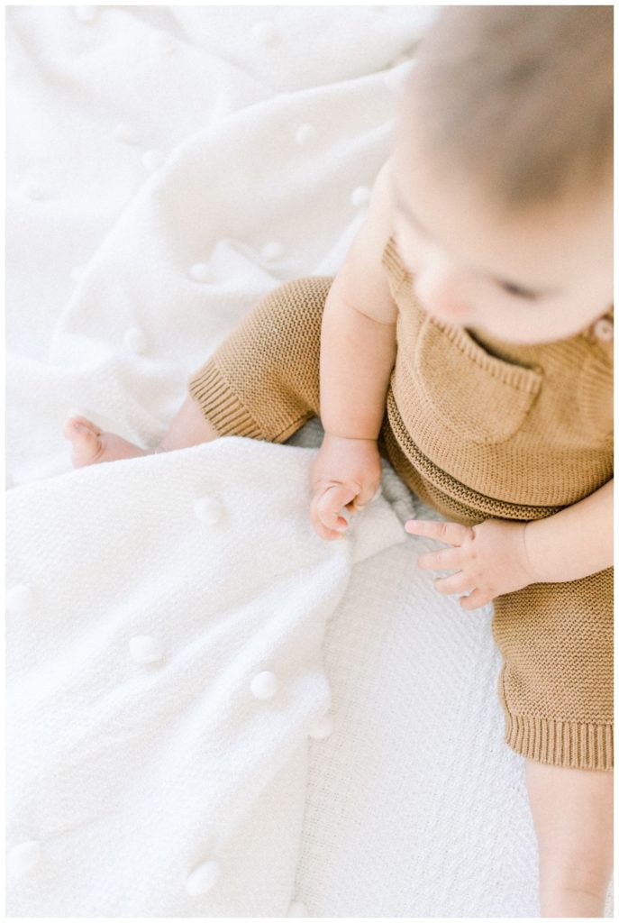 Close up photo of a nine month old boy in a copper cotton romper clutching a soft white blanket.