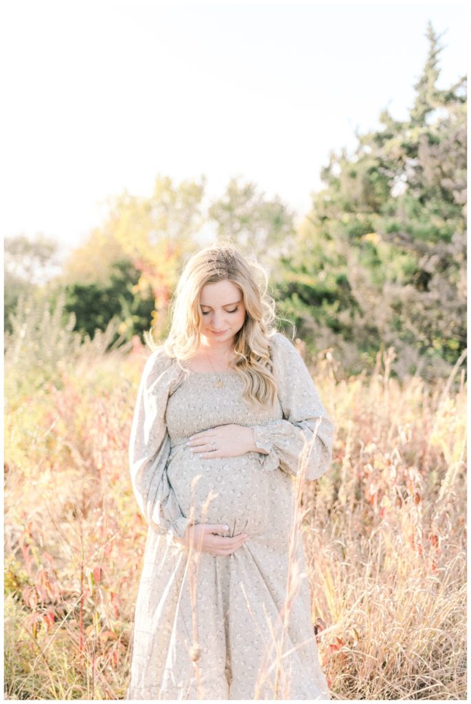 Photo of a young pregnant mom standing in sunset light looking down in a golden field.