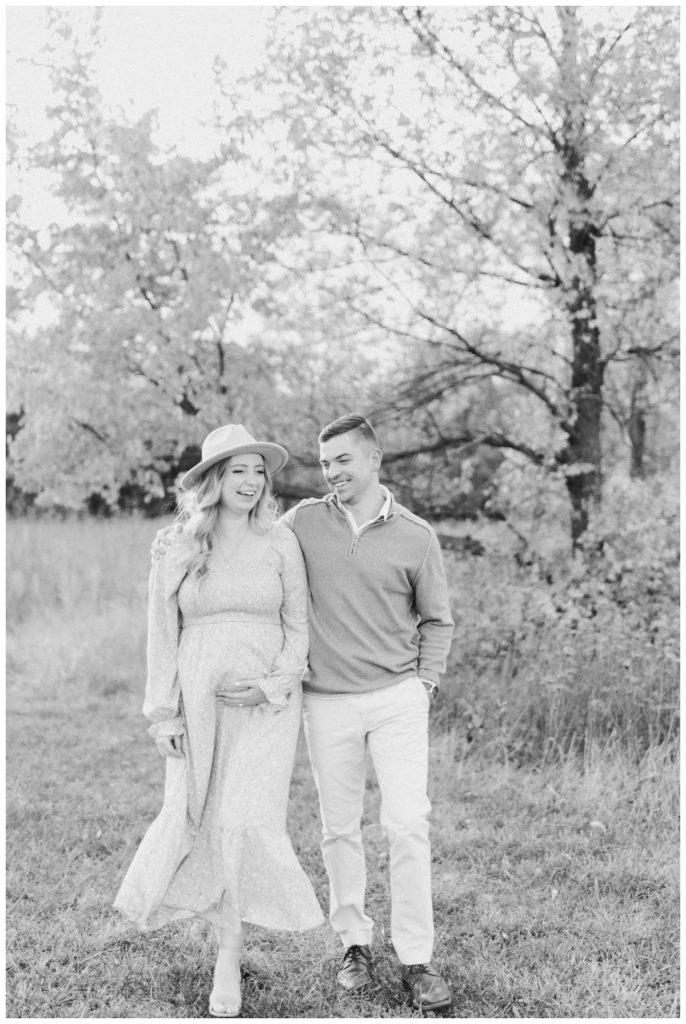 Black and white photo of a young couple walking and laughing while the young mother has her hand on her expectant stomach. 