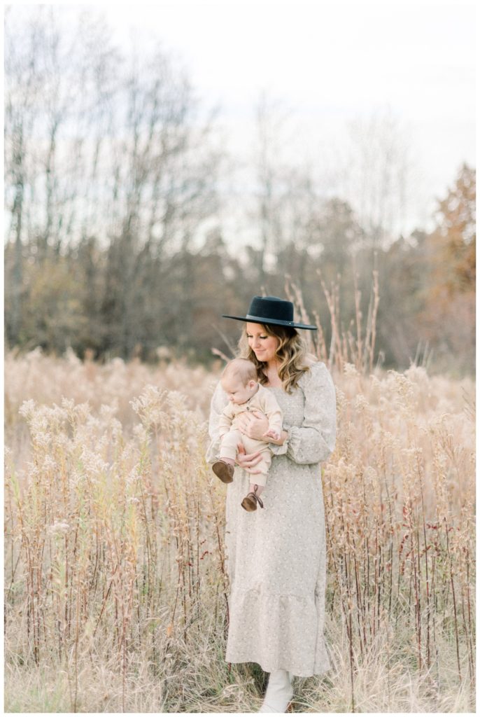 Picture of a young mom standing in a soft neutral colored wheat field holding her young son.