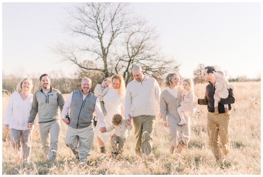 A big photo of an extended family all wearing different tones of neutral colors walking through a wheat field smiling at one another. 