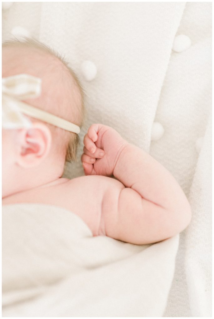 A close up photo of a newborn girl's arm and tiny fingers on top of a white polka dot blanket.